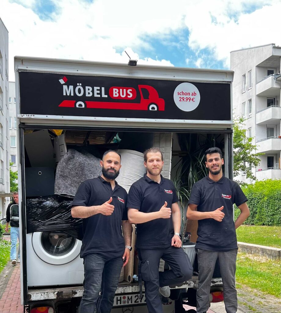 Drei Männer in schwarzer Firmenkleidung lächeln vor einem Möbeltransportfahrrad.