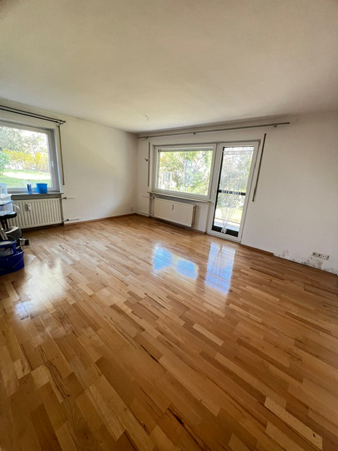 Ein leerer Raum mit Holzboden und zwei Fenstern, durch die Tageslicht fällt